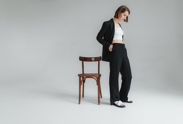 Модный снимок молодой стильной женщины в черном костюме с стулом в студии