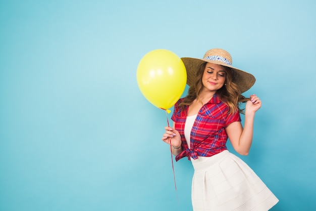 Fashion smiling young woman with yellow air balloon over colorful blue background with copyspace.