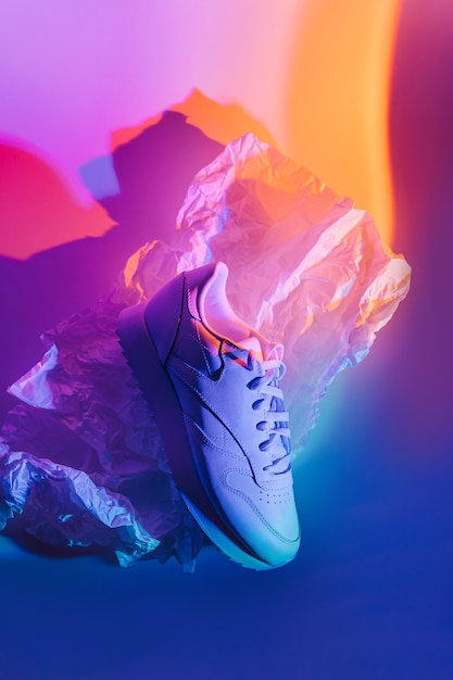 Фото Модные кроссовки на ярком абстрактном фоне. спортивная обувь в неоновом свете. синий и оранжевый градиент.