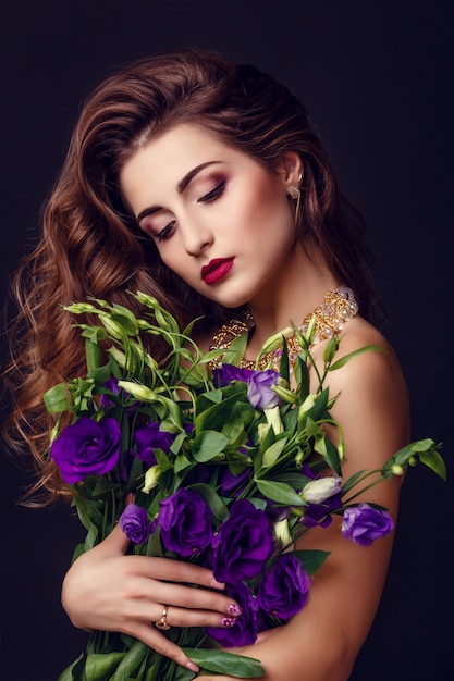 Fashion studio photo of beautiful brunette woman with bright makeup with a bouquet of purple and white eustoma