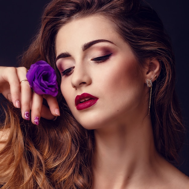 Модное студийное фото красивой брюнетки с ярким макияжем с букетом пурпурно-белой эустомы