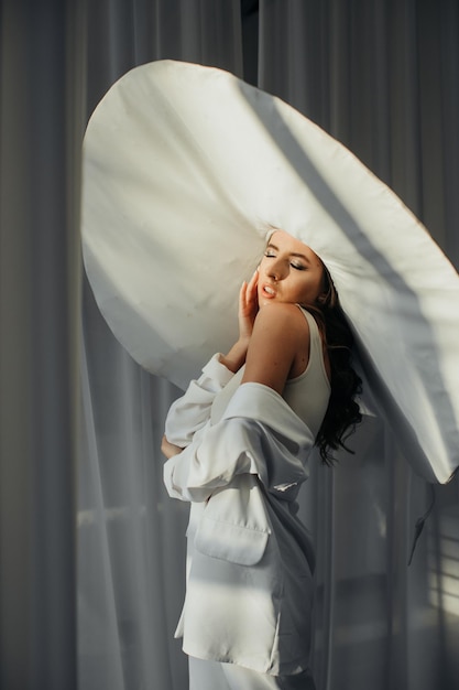 Модное студийное фото элегантной дамы в гигантской белой шляпе Здоровье и красота