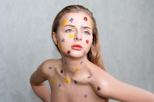 Fashion studio portrait of nude elegant lady with flowers and transparent gel on her face. Body and skin care, perfume, cosmetic concept.