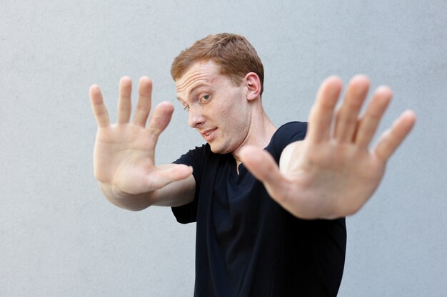 Fashion, style, emotions and people concept - Close up portrait of a redhead of a beautiful manly guy with freckles. face making frightened gesture with his palms as if trying to defend himself