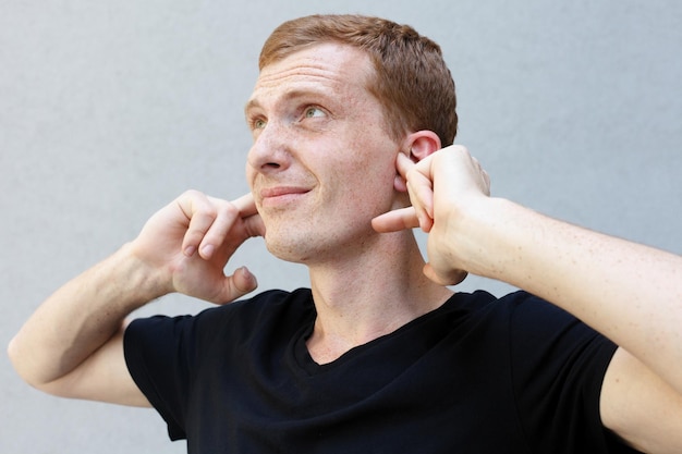 Photo fashion style emotions and people concept close up portrait of a redhead of a beautiful manly guy with freckles frowning his face closing ears with palms annoyed and tired of noise