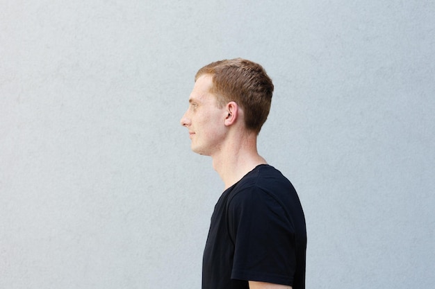 Photo fashion style emotions and people concept close up portrait of a redhead of a beautiful manly guy with freckles on a gray background black tshirt stands exactly and looks away