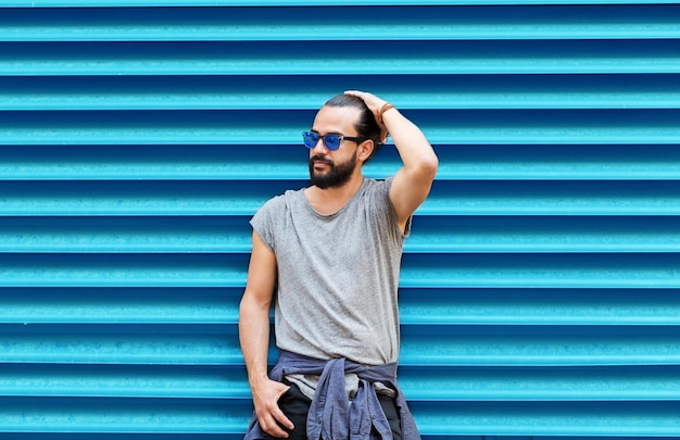 Fashion style and people concept man in sunglasses with beard posing over ribbed blue wall background