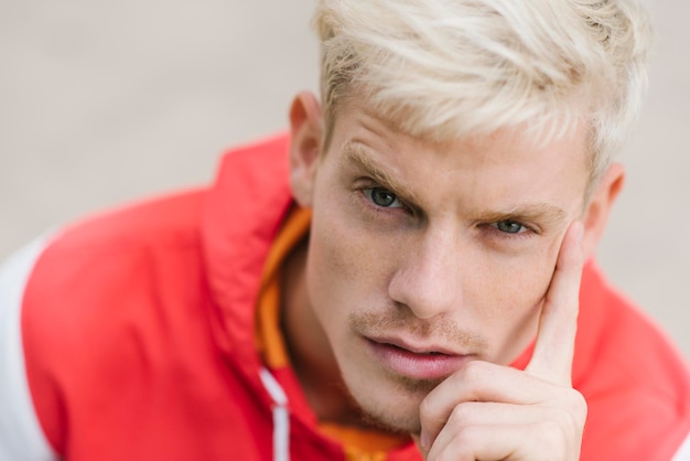 Fashion style portrait of handsome attractive blond man with serious look in outdoor Male model looking to the camera with finger on face People lifestyle concept