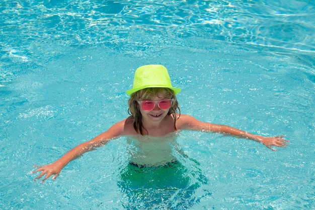 Fashion summer kids in hat and pink sunglasses Child splashing in swimming pool