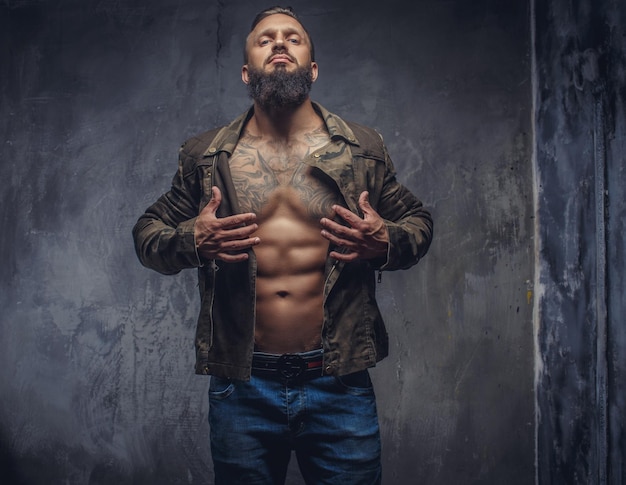 Fashion tattooed man with beard in blue jeans and jacket on nude body.