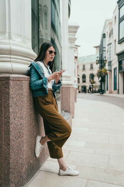 fashion teenager relies on the wall, using her cellphone and waiting for her boyfriend