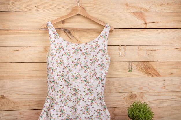 패션 트렌드 드레스는 옷걸이에 꽃무늬 프린트가 있고 나무 배경에는 귀걸이가 달려 있습니다.