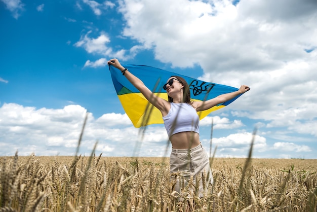 Ragazza ucraina di modo con la bandiera nazionale sul campo di grano nel periodo estivo