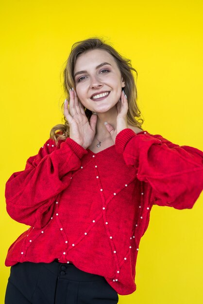 Fashion woman in classic red knitted sweater posing and smiling on yellow background. lifestyle