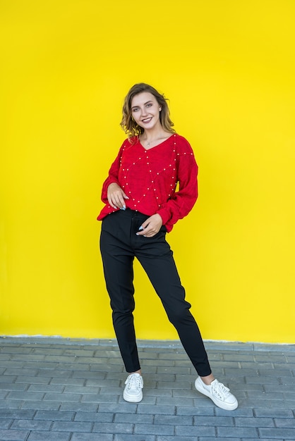 Fashion woman in classic red knitted sweater posing and smiling on yellow