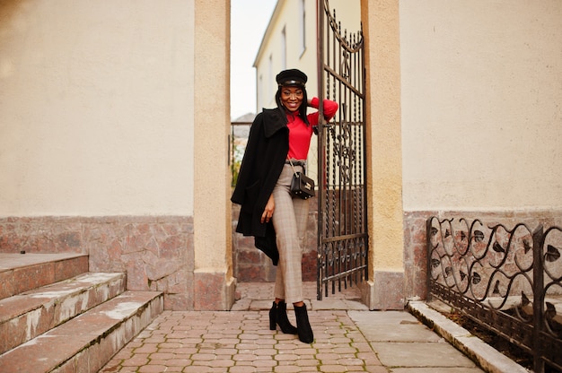 Fashion woman in coat and newsboy cap posed at street.