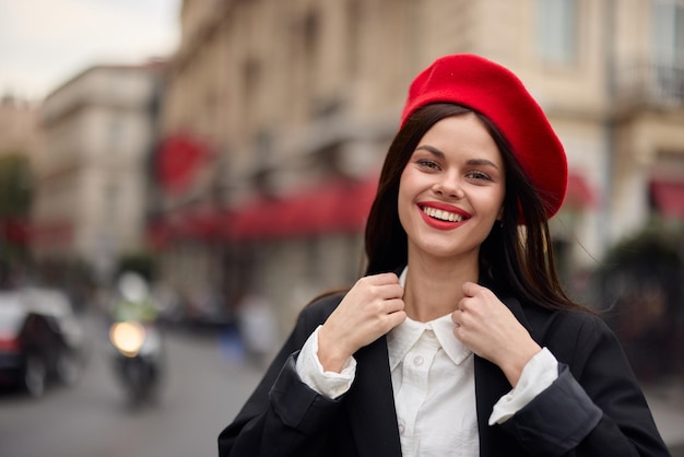 Photo fashion woman portrait smile teeth standing on the street in the city background in stylish clothes with red lips and red beret travel cinematic color retro vintage style urban fashion lifestyle