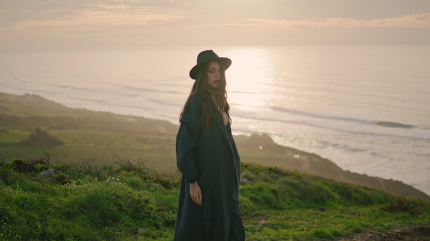 Fashion woman posing sunset wearing stylish hat model standing hill near ocean