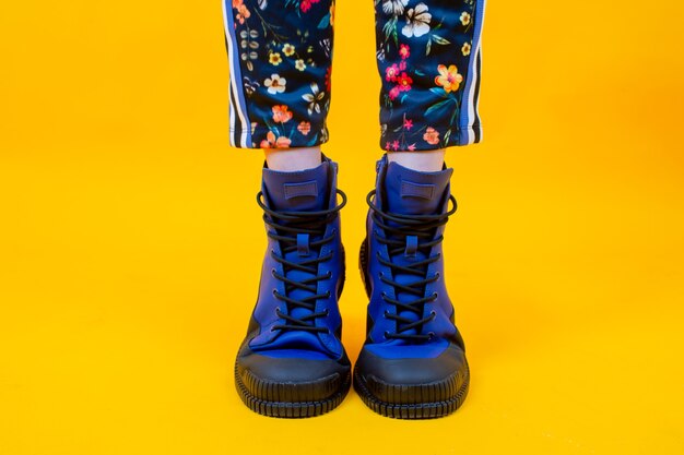 Fashion woman's legs in colorful pants and blue boots over yellow background