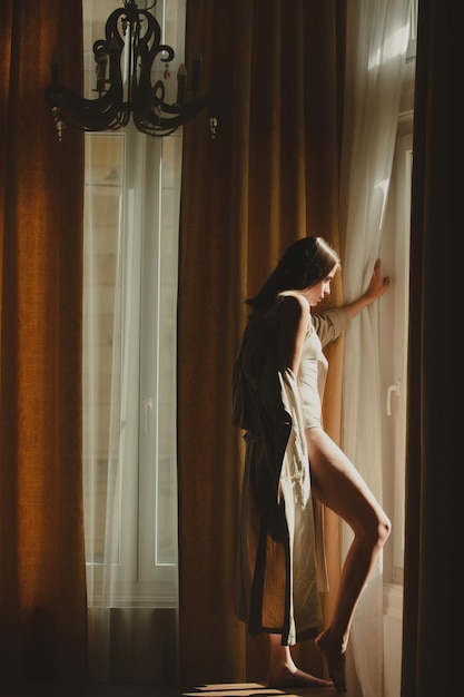 Модная женщина сексуальная и чувственная в роскошной квартире позирует на оконных шторах Сексуальная привлекательная женщина позирует с стройным сексуальным телом Красивый сексуальный портрет модели