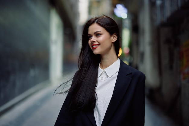 Fashion woman smile with teeth portrait tourist in stylish clothes in jacket with red lips walking down narrow city street flying hair travel French style cinematic color retro vintage style