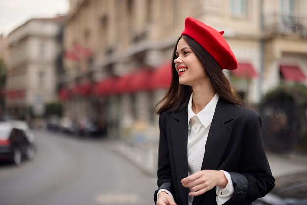 Fashion woman smile with teeth standing on the street in front of the city tourist in stylish clothes with red lips and red beret travel cinematic color retro vintage style urban fashion