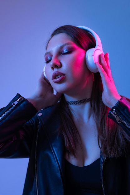 Fashion woman with headphones listening to music over neon background at studio