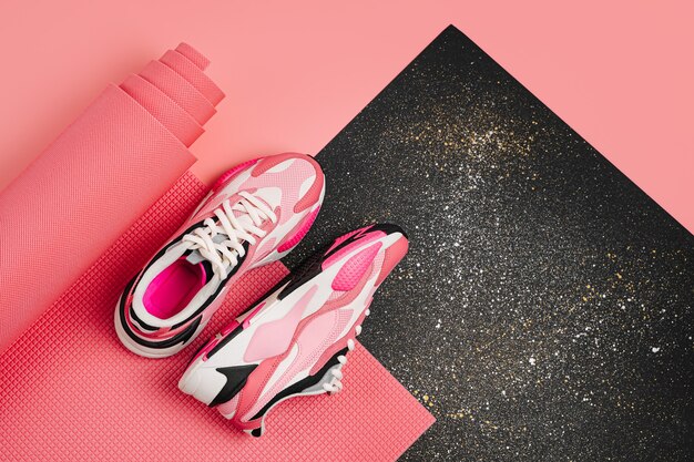 Fashion women's sneakers with a pink yoga mat on  black background. Healthy lifestyle concept.    Flat lay top view copy