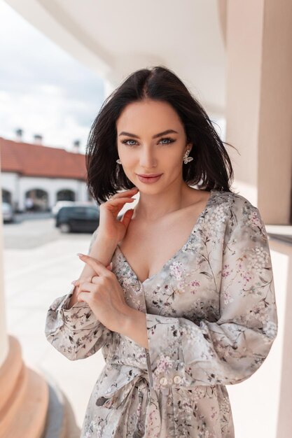 Fashion young beautiful woman with shorts hairstyle in stylish vintage spring dress walks in the city and looks at the camera