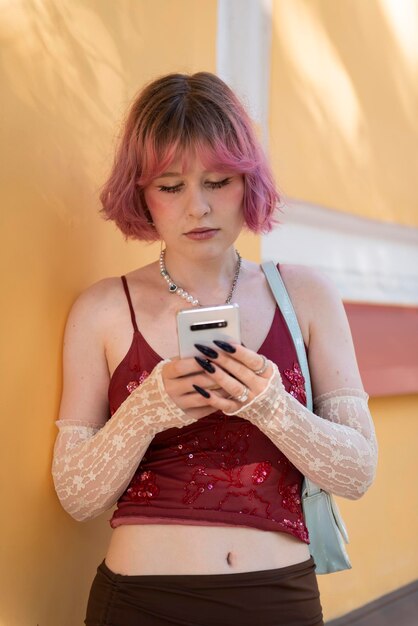 Foto moda giovane ragazza creativa capelli di colore rosa in piedi al muro con lo smartphone