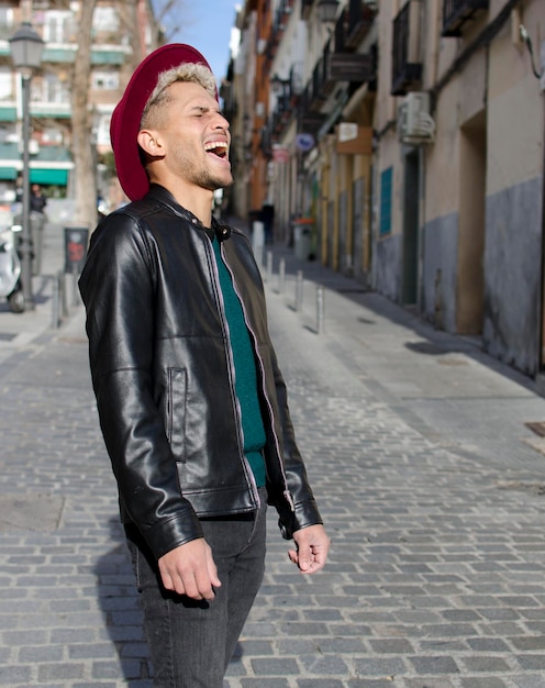 Fashion young model with leather jacket and red hat smiling in the street