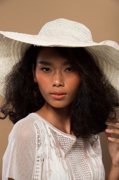 Fashion Young thin Asian Woman Tan skin eyes beautiful make up fashion white lace dress posing attractive glam look straw hat. Studio Lighting beige yellow cream Background, summer beach hot sun