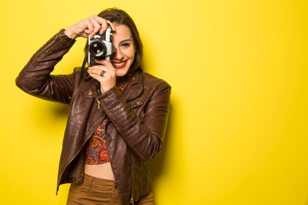 ファッションの若い女性は黄色の壁に古いカメラで写真を作る