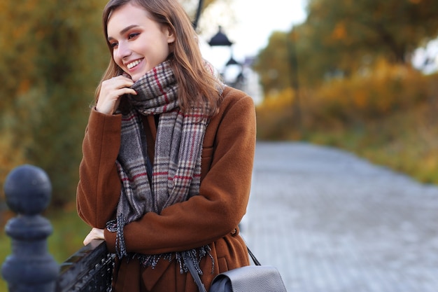 写真 コート、スカーフ、ハンドバッグを身に着けているファッションの若い女性屋外