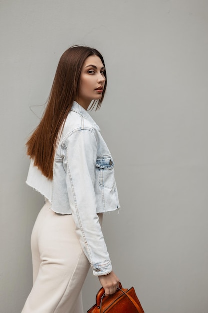 Fashion young woman in trendy denim clothes walks on the street and looks at the camera