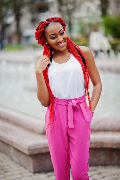 Fashionable african american girl at pink pants and red dreads posed outdoor against fountains