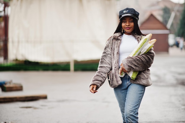 Fashionable african american woman in black cap and fur with two baguette rolls at hands