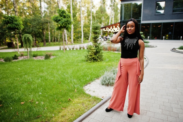 Fashionable african american woman in peach pants and black blouse pose outdoor.