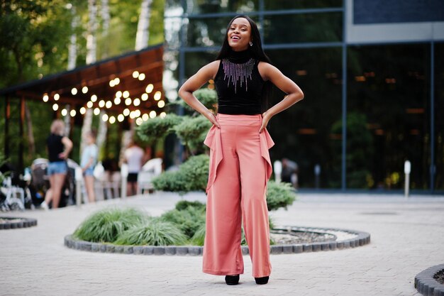 Fashionable african american woman in peach pants and black blouse pose outdoor