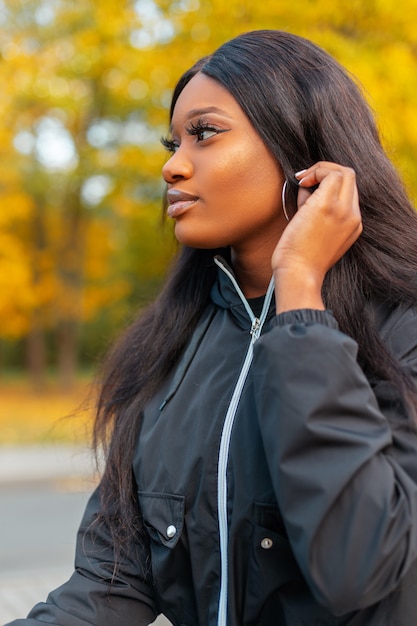 Fashionable beautiful black woman model with stylish casual jacket in park with colored autumn foliage