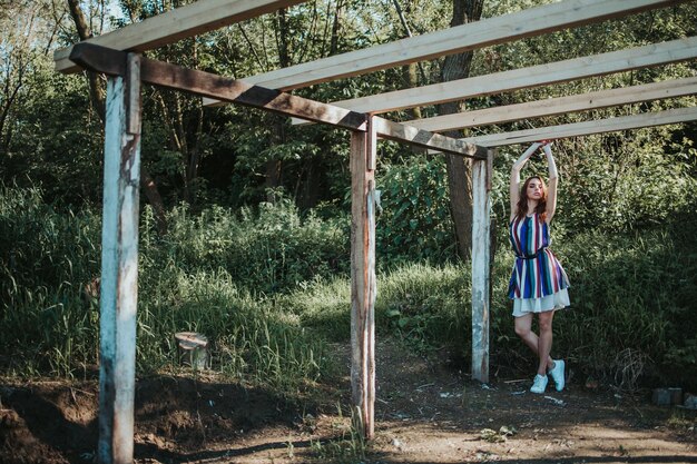 Fashionable beautiful Caucasian woman holding the wooden beam of an unfinished house in the woods