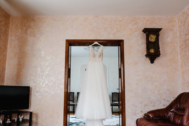 部屋のハンガーにぶら下がっているファッショナブルな美しい古典的なレースのシルクの花嫁のドレス。朝の準備結婚式のコンセプト。ヴィンテージガウン。