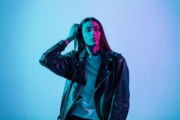 Fashionable beautiful color portrait of a young stylish pretty woman in a fashionable leather jacket in the studio with a multicolored blue pink lights