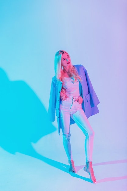 Fashionable beautiful elegant business woman in a stylish blue blazer with a white blouse and jeans in the studio on a bright colorful neon pink light