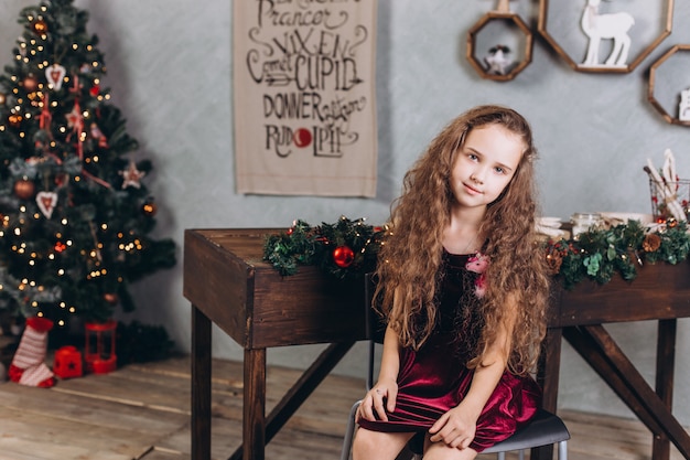 Fashionable beautiful girl in dress at home near new year eve and christmas decorations and colorful lights