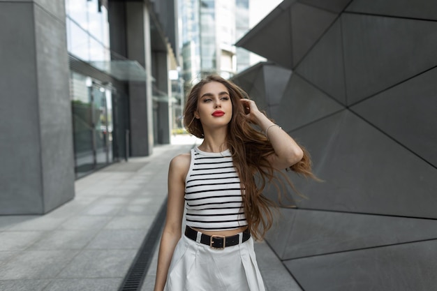 Fashionable beautiful happy woman with red lips in trendy fashion summer urban clothes walking in the city