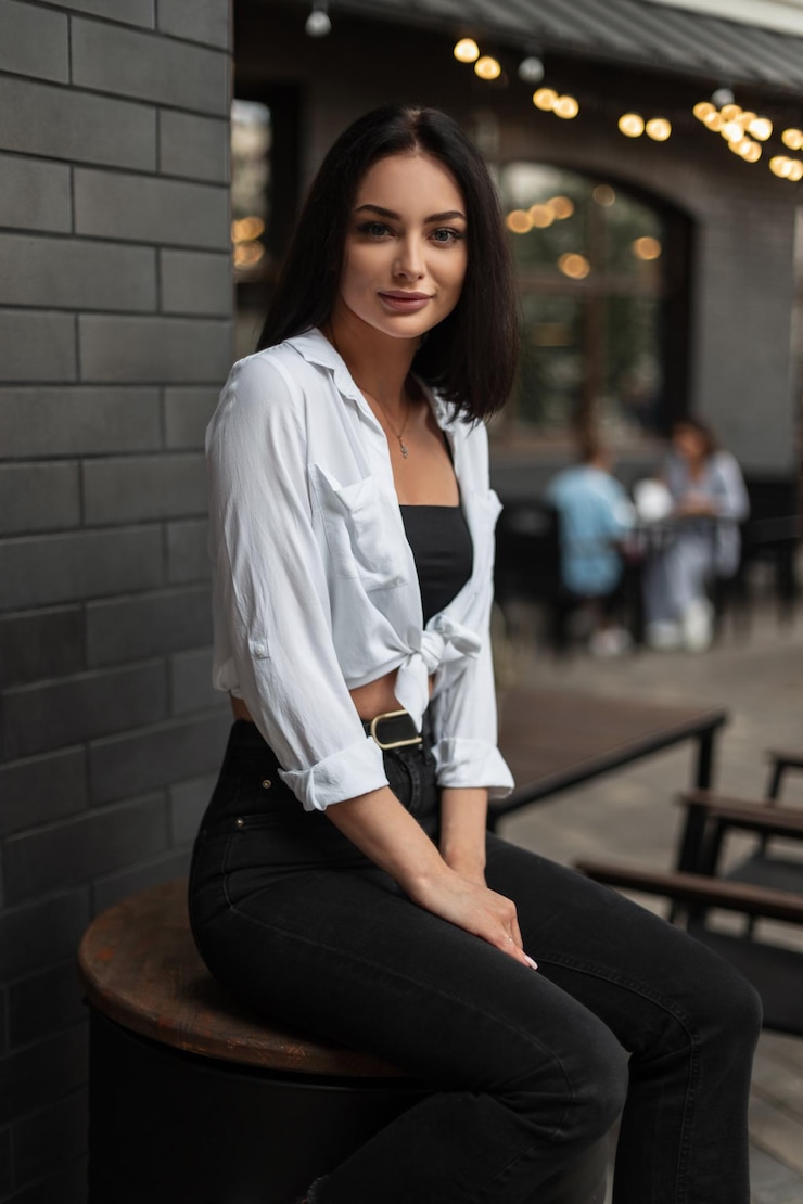 Photo fashionable beautiful urban business girl in stylish clothes with a white shirt black jeans and top sits on a black barrel in the city with lights bokeh