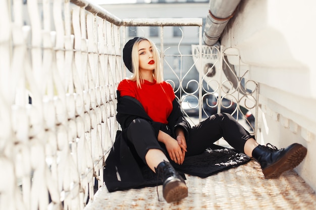 Fashionable beautiful woman in stylish black autumn clothes sits on a metal staircase