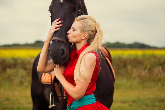 Fashionable blonde woman riding a horse in sunny day