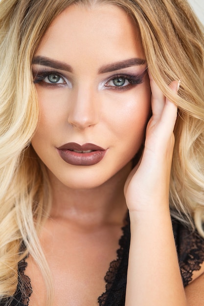 Fashionable blonde woman with perfect makeup and wave hair over a grey background. Closeup portrait